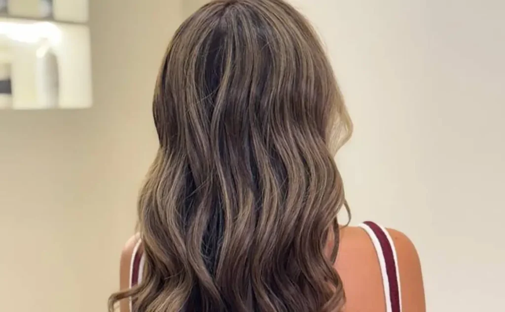 Back view of a woman's long, wavy brunette hairstyle featuring a seamless blonde balayage hair color and fresh haircut at Moiselle salon Bali, a top salon Canggu.