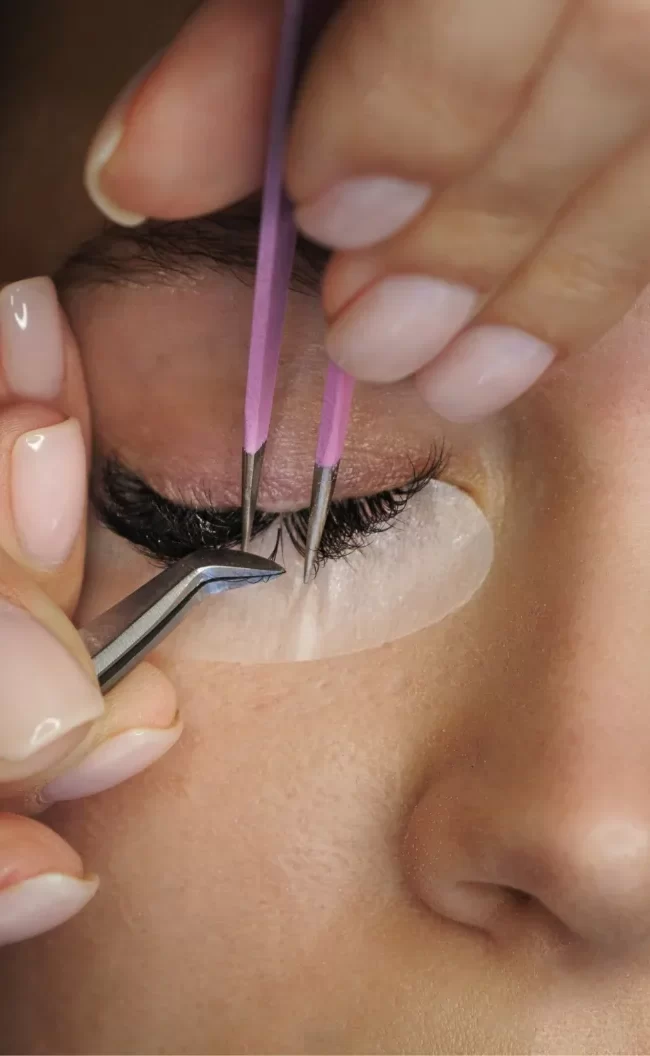 Close-up of a professional eyelash technician applying custom lash extensions Bali using precision tweezers on a client at Moiselle salon, a premium beauty lounge in Canggu.